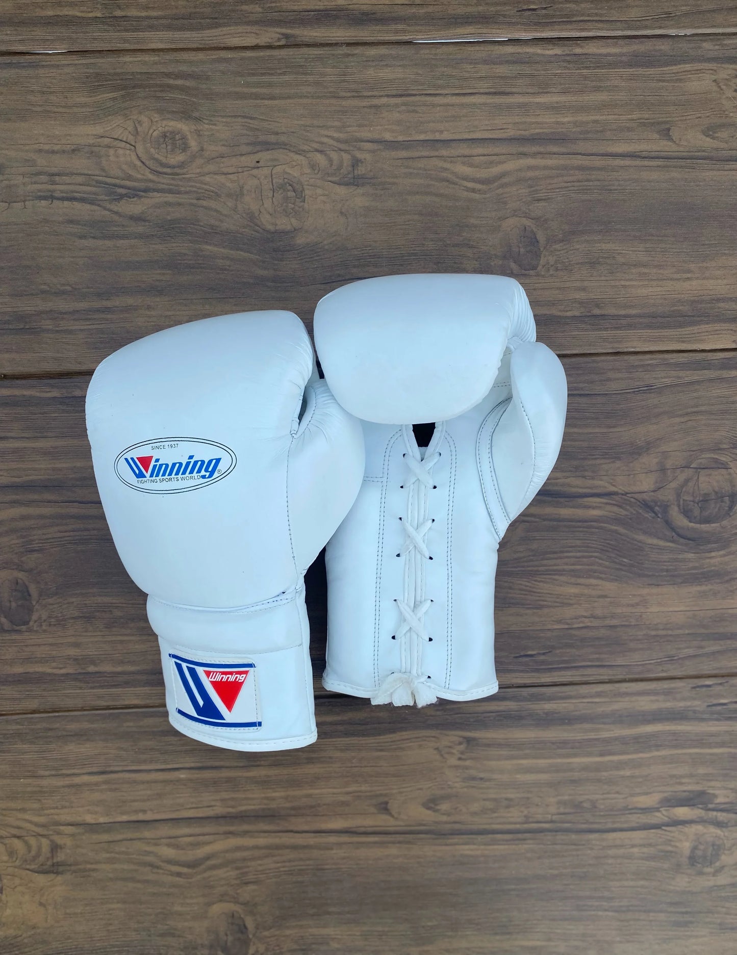 Pair of white boxing gloves with a Winning brand logo on a wooden background